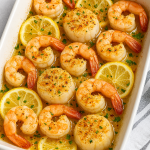 Oven-baked shrimp and scallops in a white baking dish with lemon slices, golden breadcrumb topping, and fresh parsley garnish.