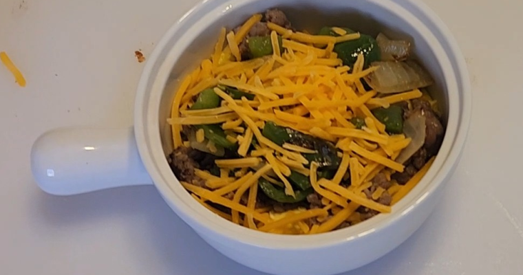 A warm keto breakfast bowl filled with browned sausage, fluffy scrambled eggs, sautéed onions and peppers, and melted cheese, arranged in a rustic ceramic bowl on a wooden surface.